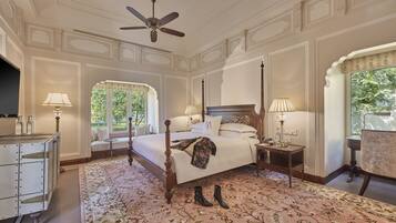 A spacious bedroom with a four-poster bed, a ceiling fan, and a large window providing a view of the outdoors.