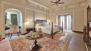 A hotel room with a large bed, a round table with breakfast, a desk, and a chair.