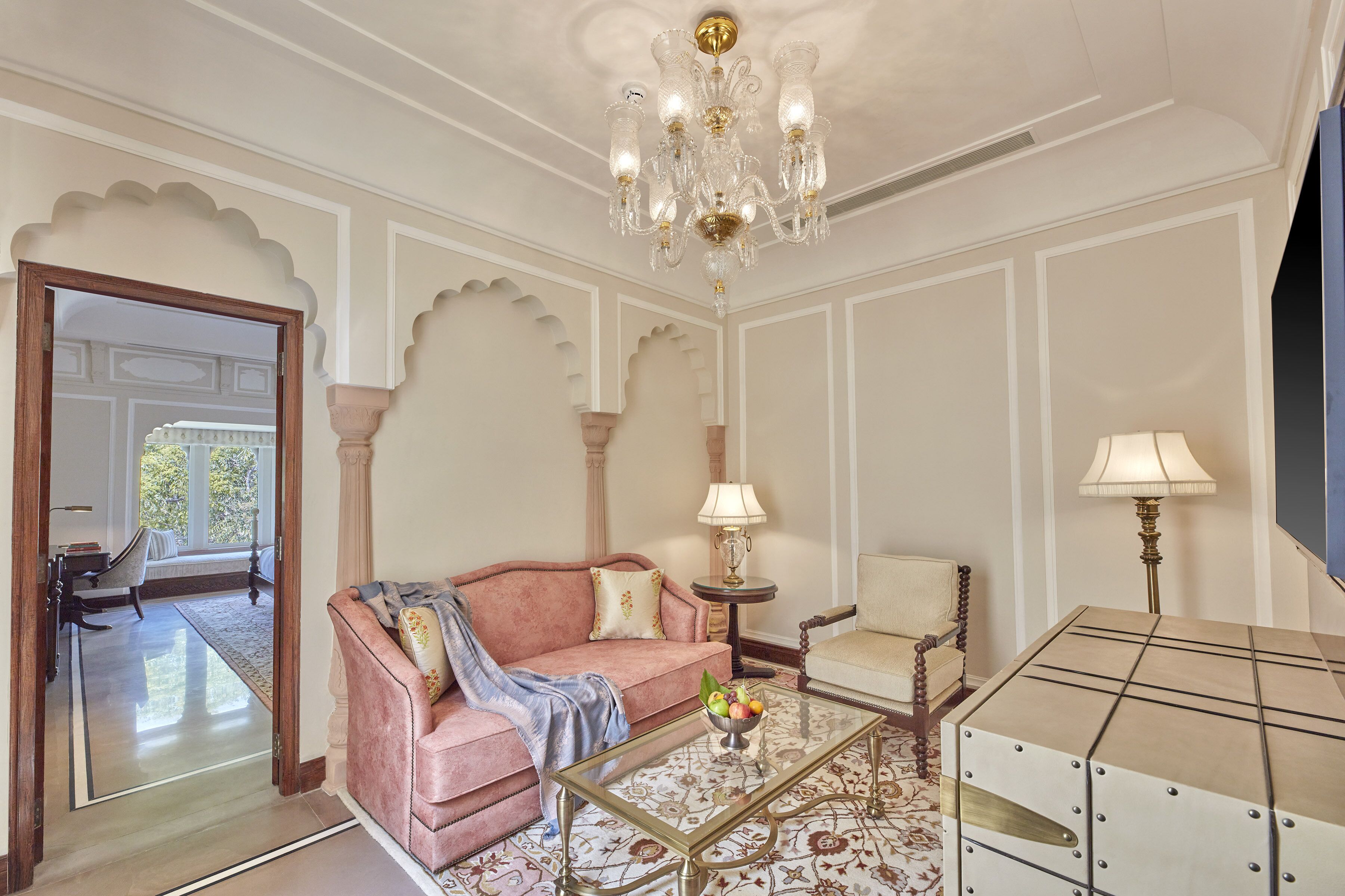 A spacious living room with a pink sofa, a glass coffee table, a chandelier, and a television.