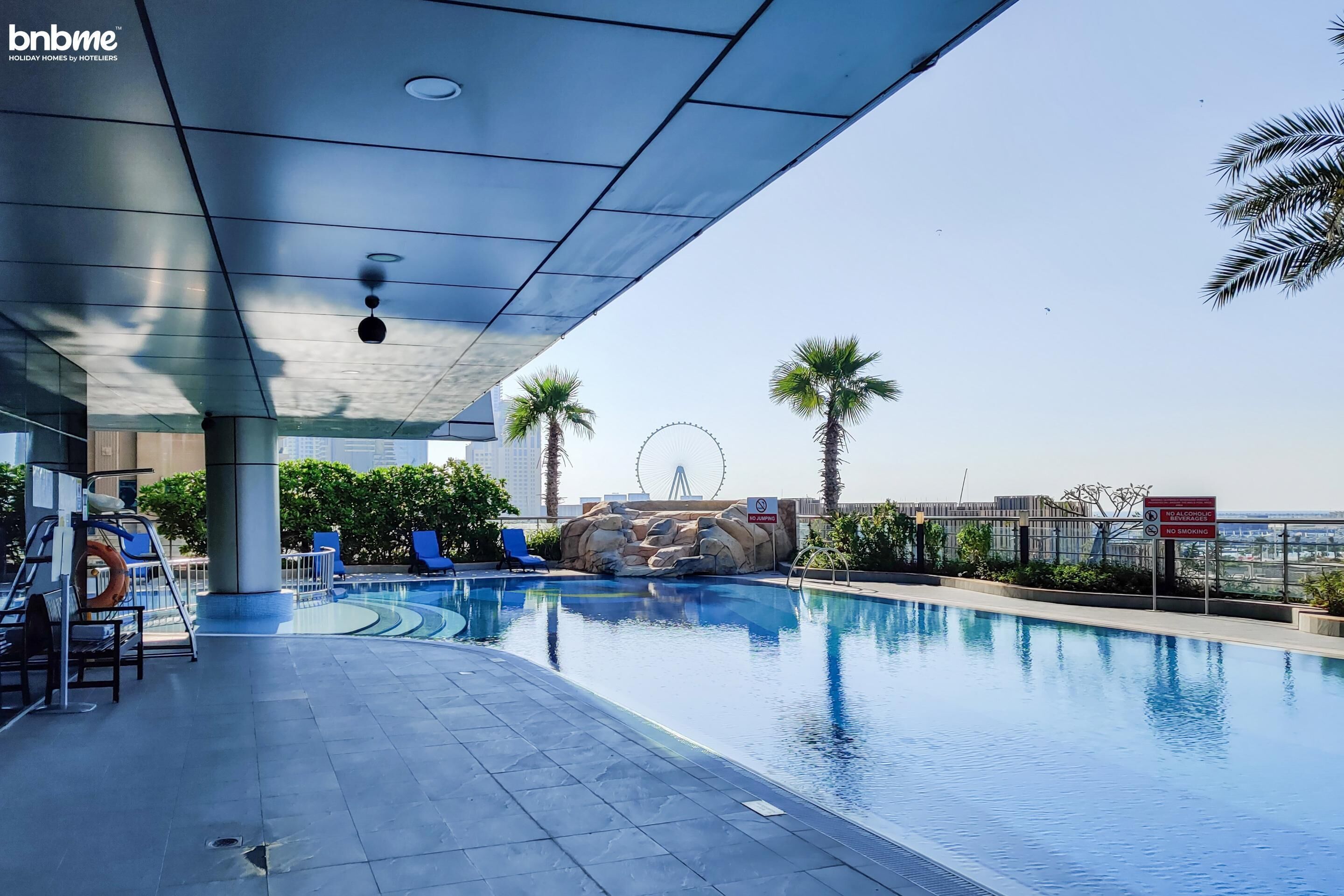 A swimming pool with lounge chairs, a Ferris wheel in the background, and palm trees.