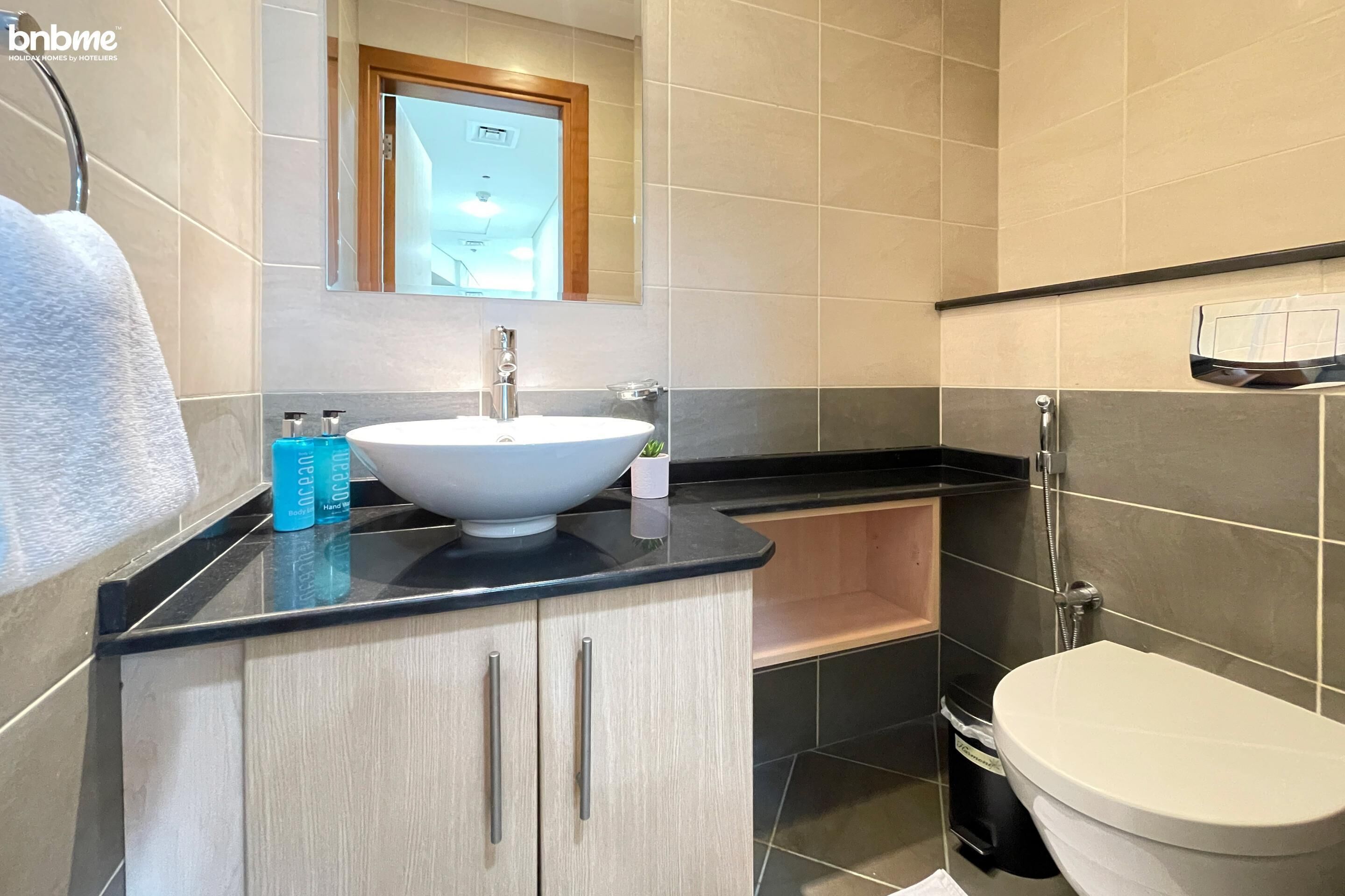 A modern bathroom with a white sink, a mirror above it, and a toilet. There are two blue bottles on the counter.