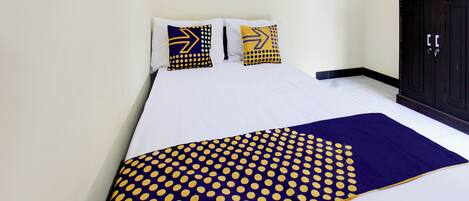 A bed with white bedding, two pillows with geometric patterns, and a blue and yellow polka dot blanket.