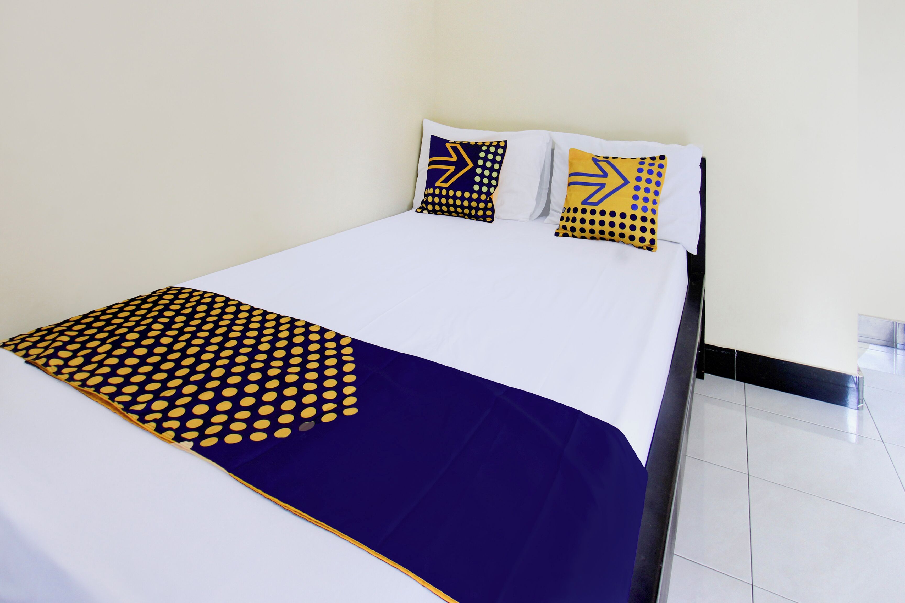 Una cama bien hecha con un edredón y almohadas a juego de lunares azules y amarillos.