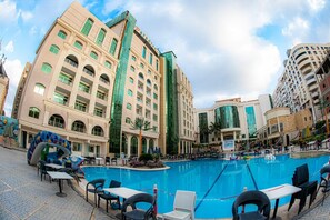 A hotel with a large pool area, outdoor seating, and a modern building facade. - paradise home city stars (Cairo)