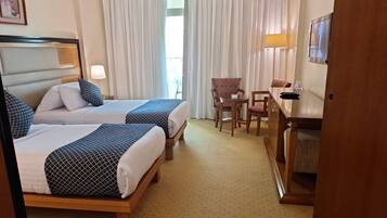Une chambre d’hôtel avec deux lits, un bureau, des chaises, une télévision et une fenêtre avec des rideaux.