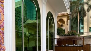 A modern outdoor seating area with wicker furniture and a wooden table, surrounded by large arched windows and a view of a building with glass facade. - paradise home city stars (Cairo)