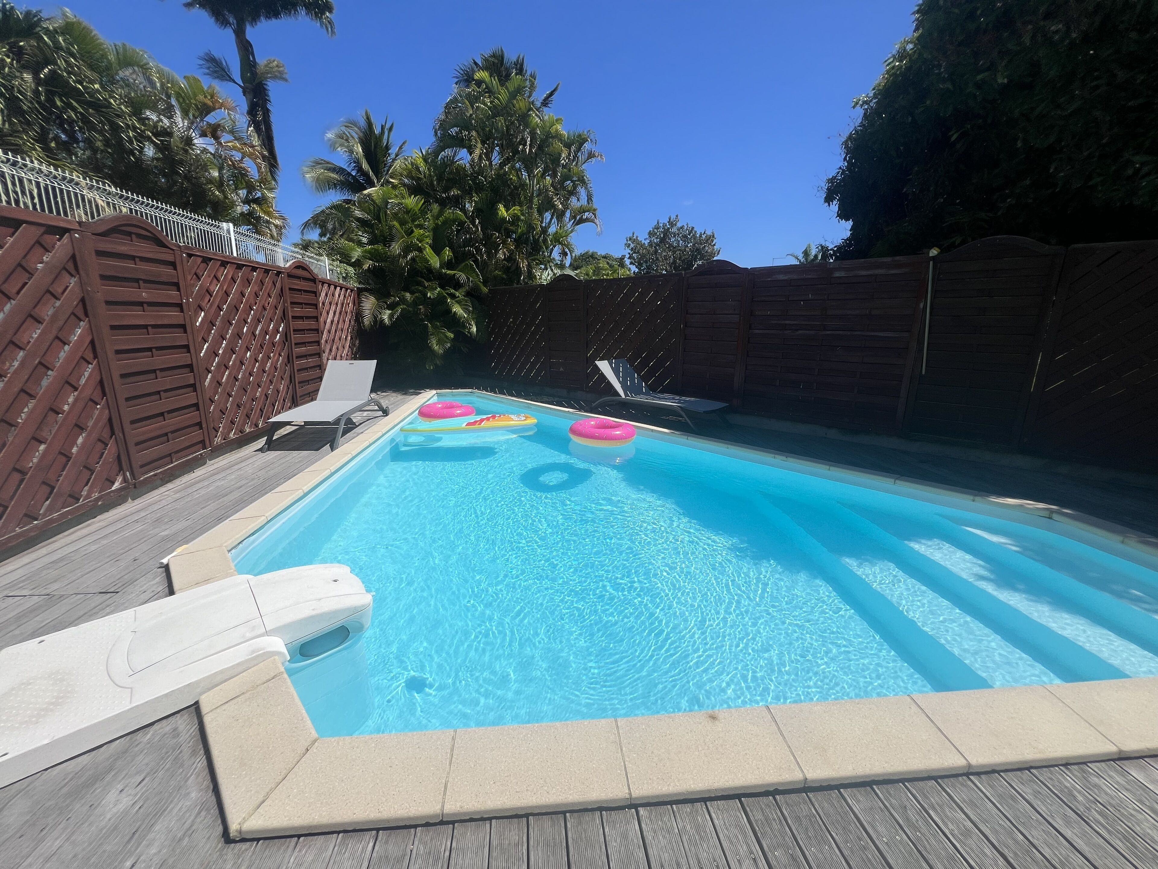 Una piscina rectangular con agua azul cristalina, rodeada por un muelle de madera y una cerca de madera.
