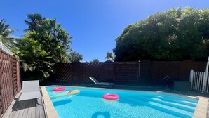 Piscina no quintal com dois flutuadores rosa, um deck de madeira e cerca de madeira.