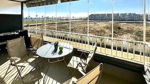 A balcony with a table and chairs, a TV, and a view of a cityscape and dry field. - Apartment in Roquetas near the Beach (Roquetas de Mar)