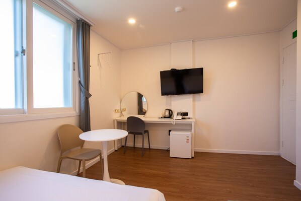 A compact hotel room with a bed, a small desk with a chair, a television, and a compact refrigerator.
