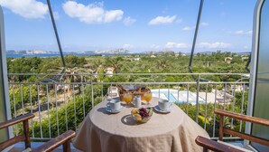 Un balcón con una mesa lista para el desayuno, con vistas a una piscina y un paisaje pintoresco.