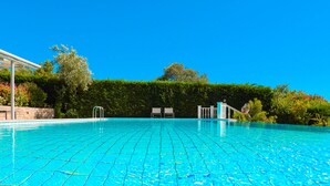 Una piscina azul cristalina con diseño de cuadrícula, rodeada de exuberante vegetación y una cerca blanca.