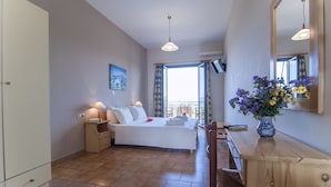 Un dormitorio con cama, mesitas de noche, escritorio, silla, un florero con flores, un cuadro y un ventanal grande.