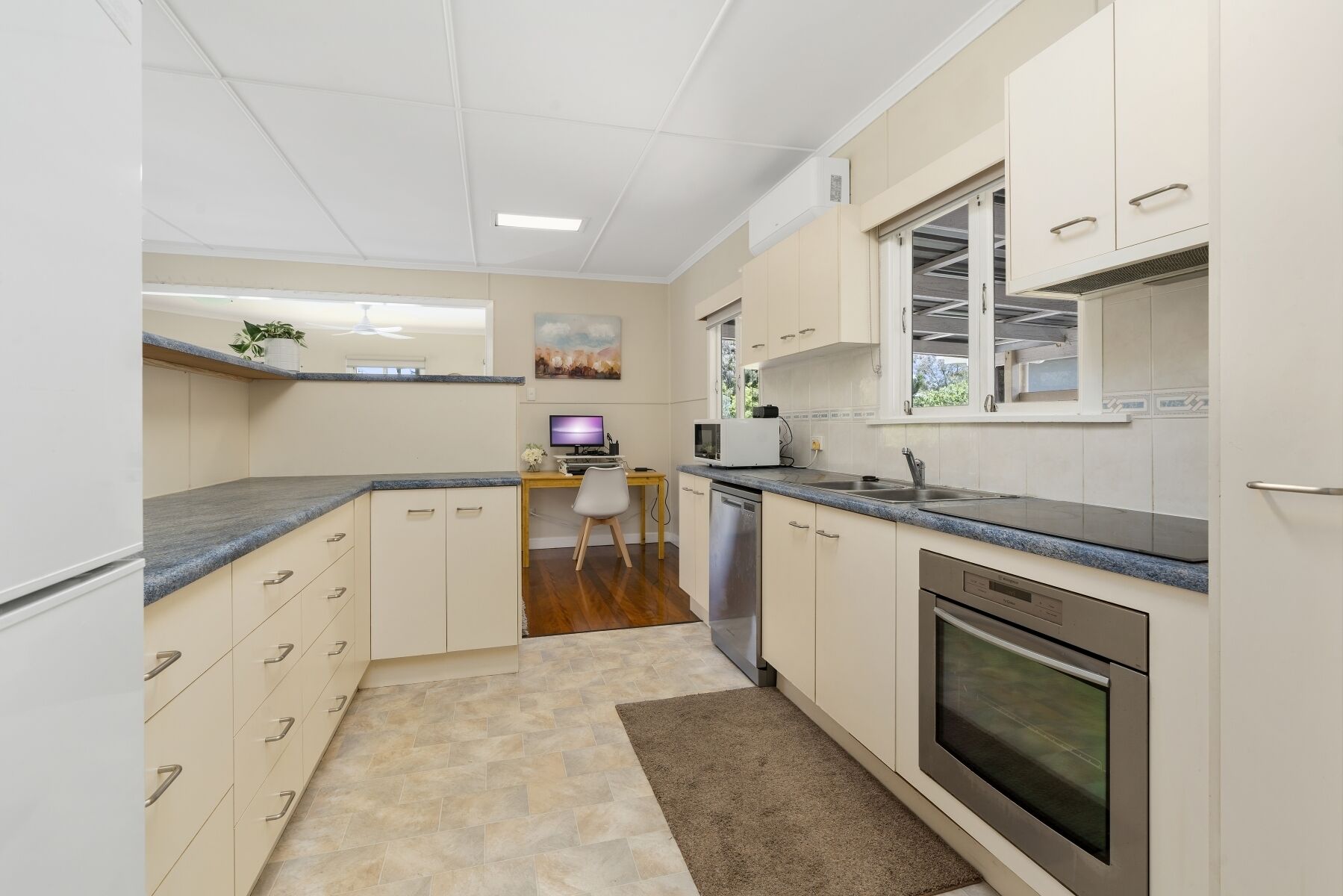 A compact kitchen with white cabinets, a granite countertop, a built-in oven, and a small dining area with a computer and chair.