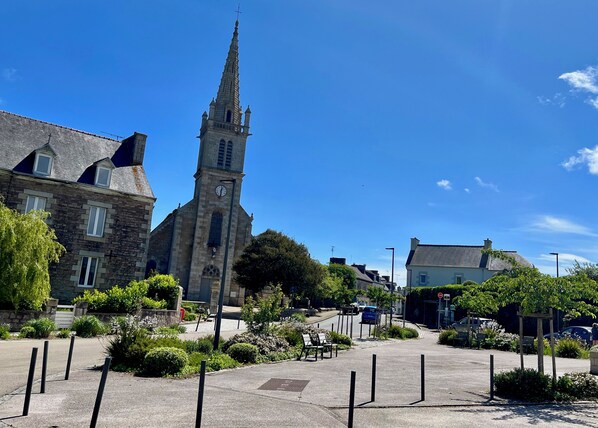 A church with a tall spire and a clock tower, surrounded by a small town square with benches and greenery.