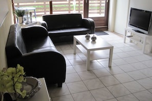 A living room with a black sofa, a white coffee table, and a TV on a stand. - 1 from Fam. Moritz Koopman (Petten)