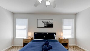 Une chambre dotée d’un grand lit, de deux tables de chevet, d’un ventilateur de plafond et d’une œuvre d’art accrochée au mur.