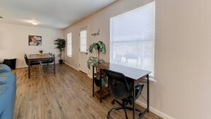 Un vaste salon doté d’un plancher en bois, un coin repas avec une table et des chaises, et de grandes fenêtres équipées de stores.