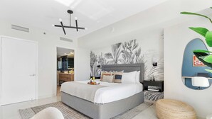 Un dormitorio moderno con una cama grande, una mesita de noche, una silla, un taburete redondo y una pared decorada con un mural botánico.