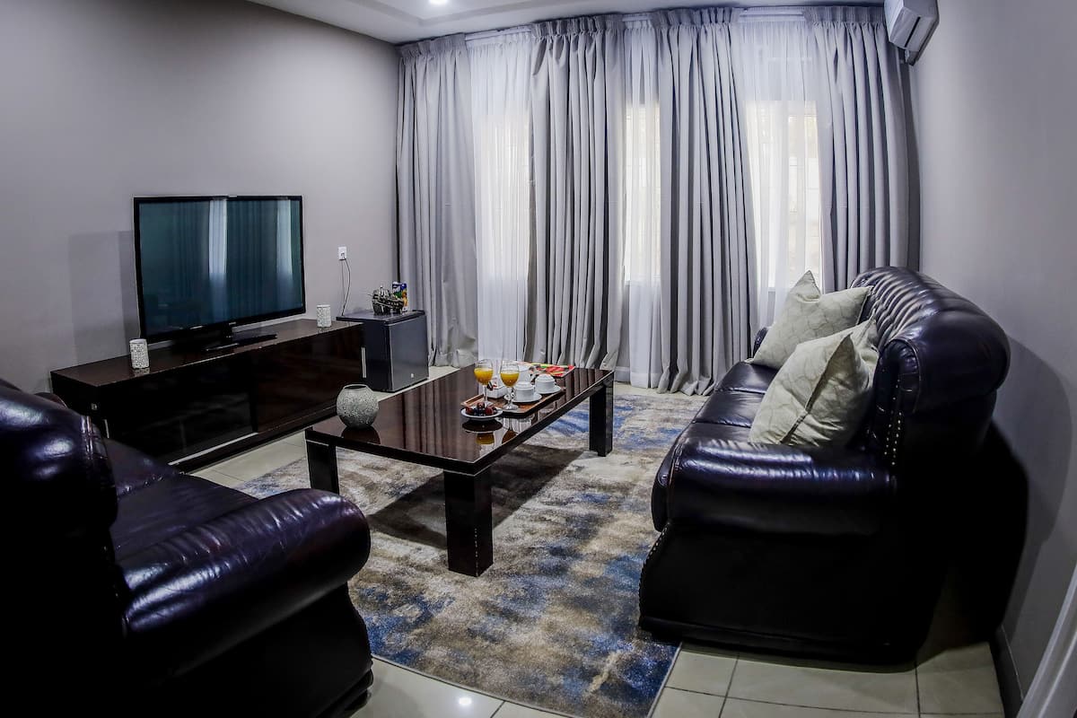 Una sala de estar moderna con un televisor de pantalla plana, sofás de cuero, una mesa de centro y un ventanal con cortinas.