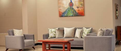 A living room with a grey sofa set, a wooden coffee table, and a peacock painting on the wall.