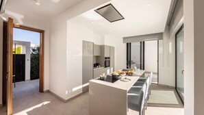 A modern kitchen with a central island, large windows, and a view of the outdoors. - Protaras Periyiali Seaside Villa 33 (Paralimni)