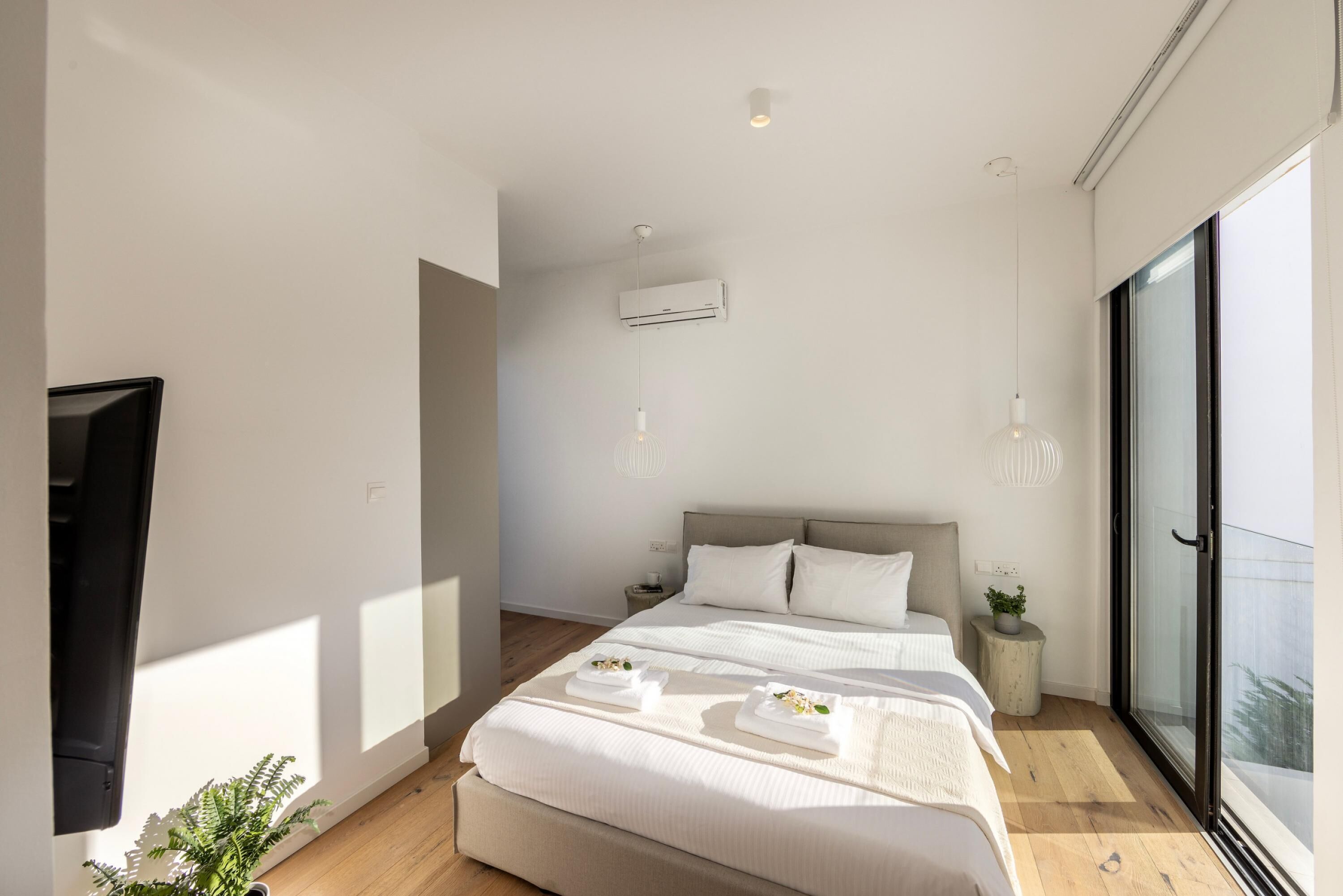 A modern bedroom with a large bed, bedside tables, and a sliding glass door to a balcony.