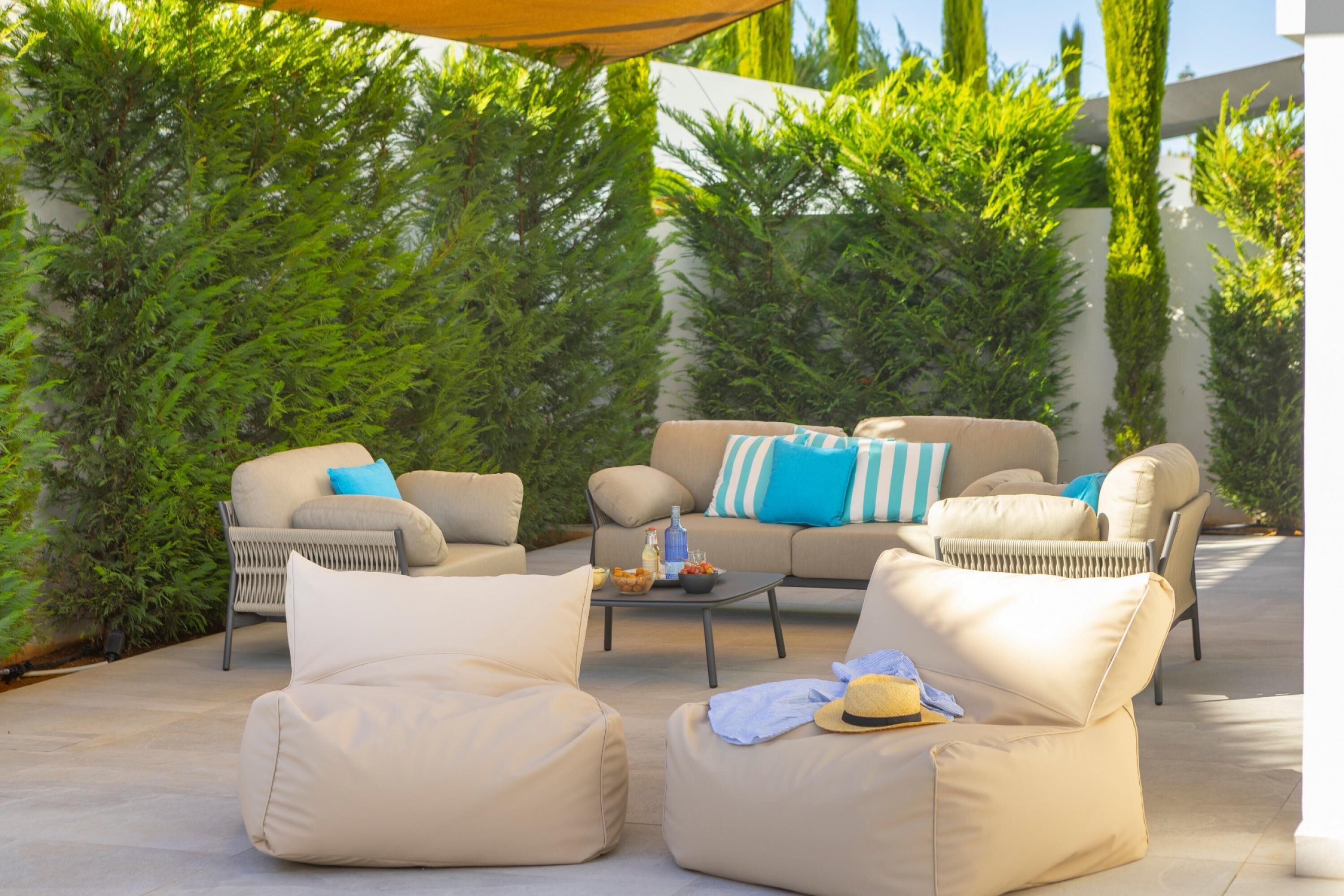 An outdoor seating area with cushioned chairs and a sofa, a small table with a bottle and bowl, and a yellow hat on one of the chairs.