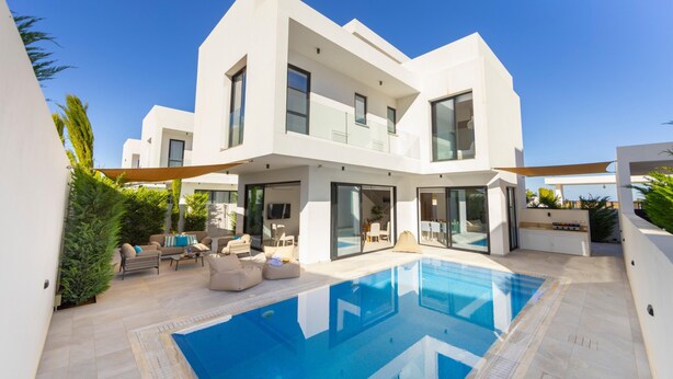 A modern two-story house with a swimming pool, outdoor seating, and large windows. - Protaras Periyiali Seaside Villa 33 (Paralimni)