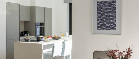 A modern kitchen with white cabinetry, a dining area with a table set for two, and a framed abstract artwork on the wall.