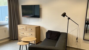 A modern living room with a sofa, a TV mounted on the wall, a small wooden table, and a floor lamp. - Apartment 170 (Bad Münstereifel)