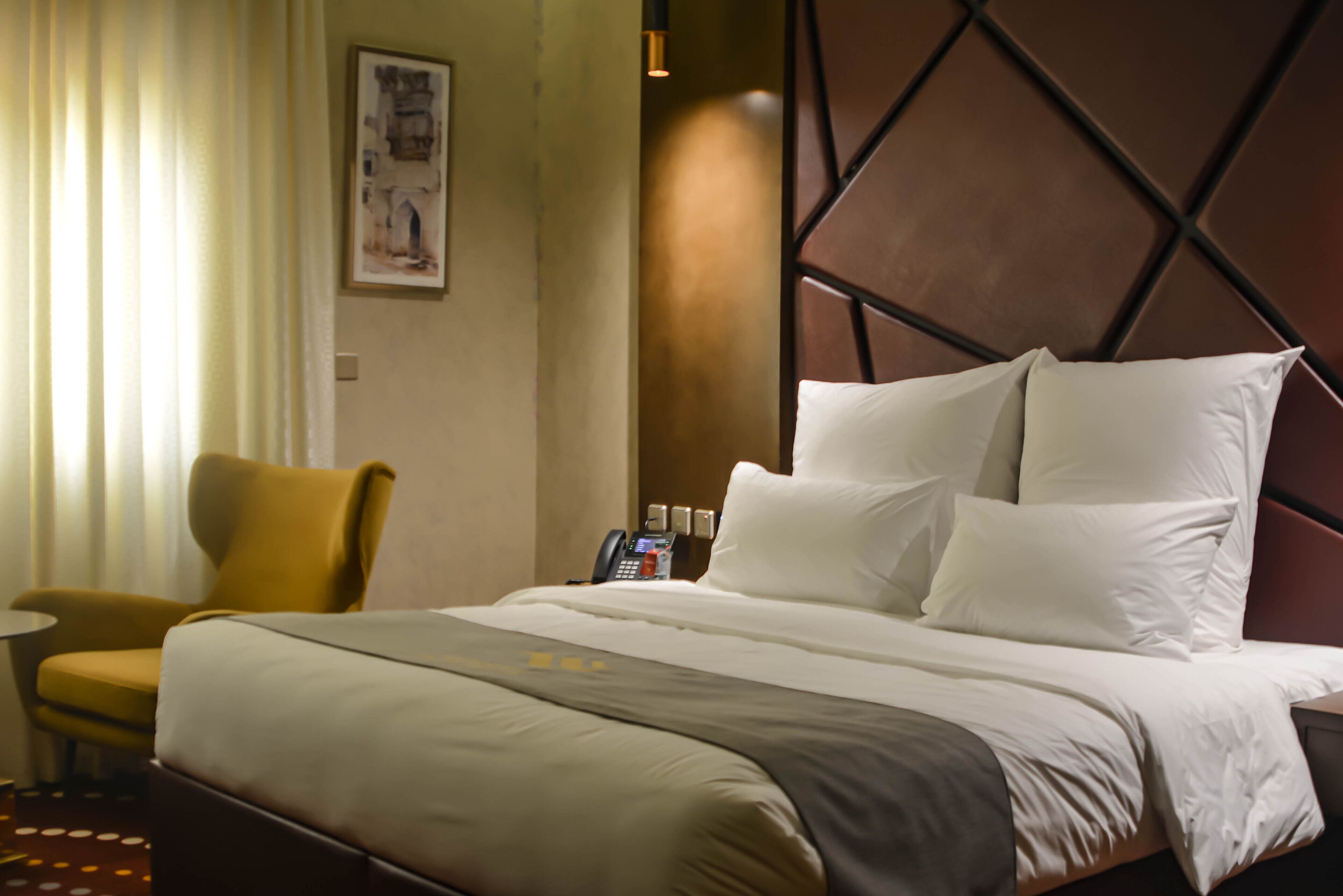 A hotel room with a bed, a chair, a small table, and a telephone.