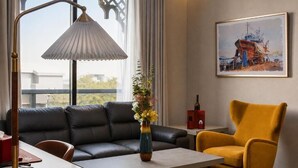 A modern living room with a sofa, a yellow armchair, a table, a vase with flowers, a lamp, a painting, and a window with a view. - Redwaves Hotel (Jeddah)