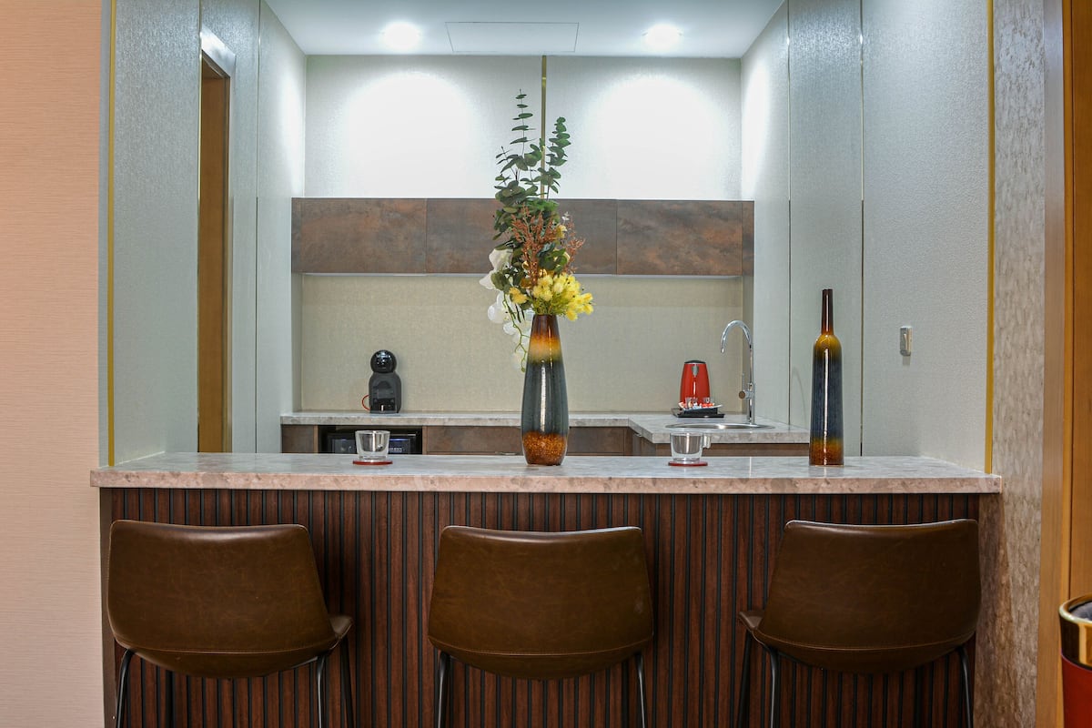 Una cocina moderna con una isla central, tres taburetes de bar y un jarrón con flores.
