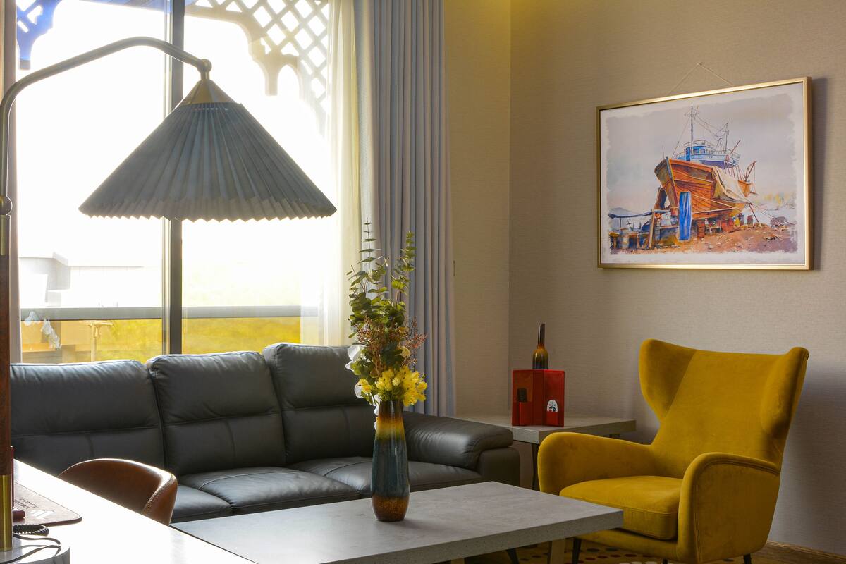 Una sala de estar moderna con un sofá, un sillón amarillo, un jarrón con flores, una lámpara y un cuadro en la pared.