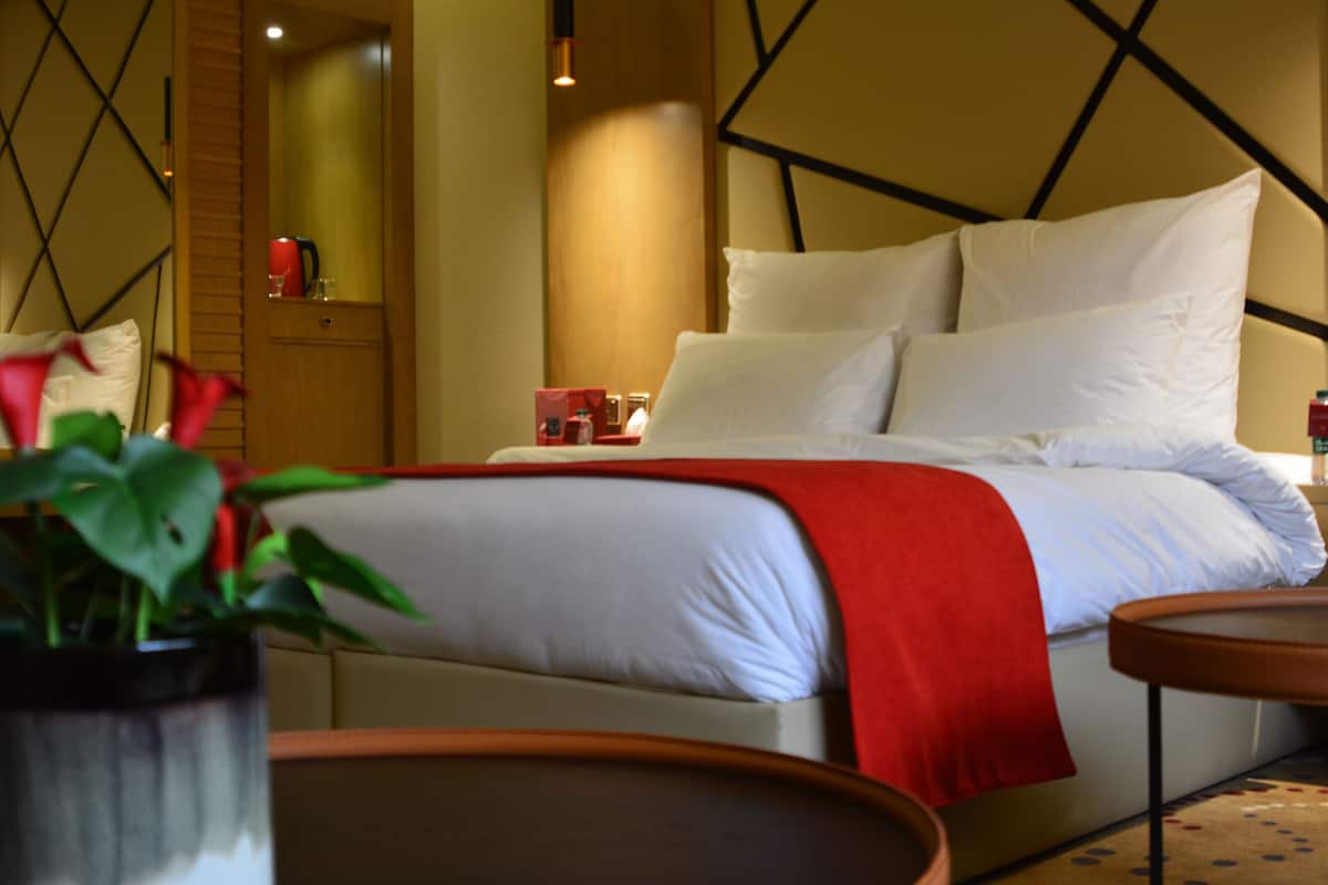 Una habitación de hotel moderna con una cama, una mesita de noche, una manta roja y una planta en maceta.