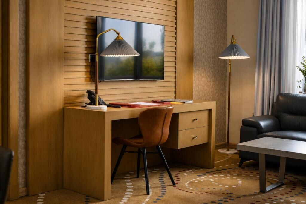 A modern room with a wooden desk, a television mounted on the wall, a black leather sofa, and a patterned carpet.