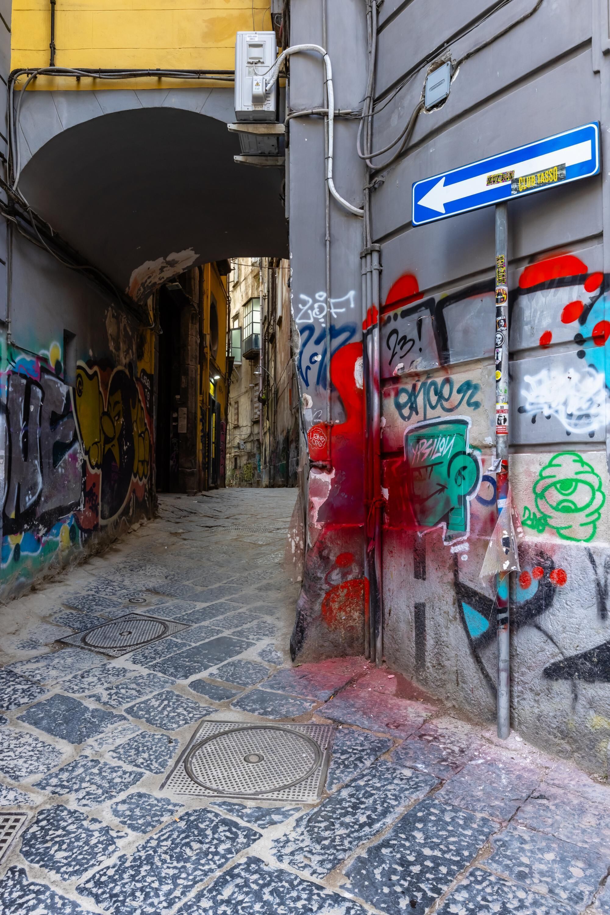 A narrow alleyway with graffiti on walls and a blue directional sign.
