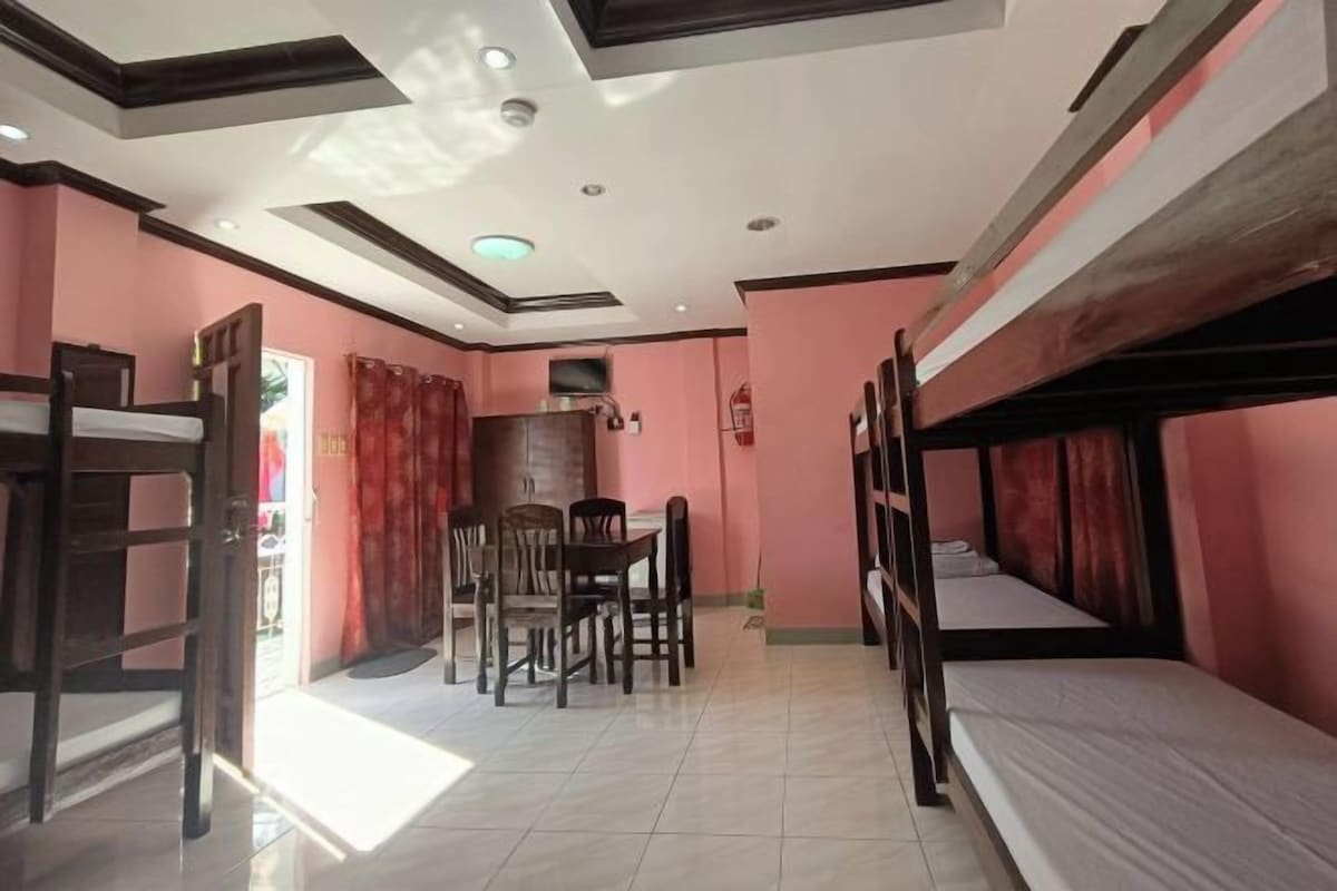 A dormitory room with bunk beds, a dining table with chairs, and a ceiling with recessed lighting.