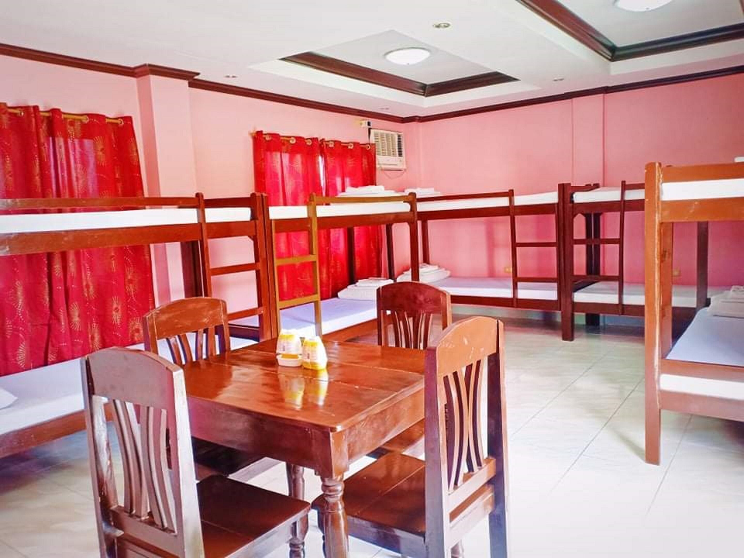 Una habitación con literas, una mesa, sillas y cortinas rojas.