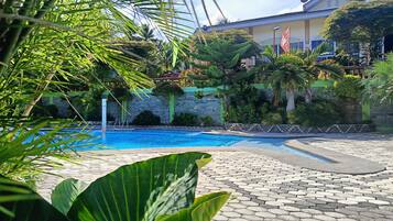 A swimming pool with a stone pathway, surrounded by lush greenery and a stone wall.
