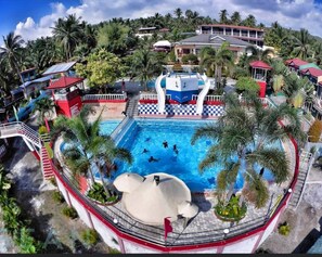 A large swimming pool surrounded by palm trees and a building with a red roof.