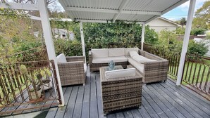 Une terrasse extérieure couverte, aménagée avec des meubles en osier, notamment un canapé et deux petites tables d’appoint.