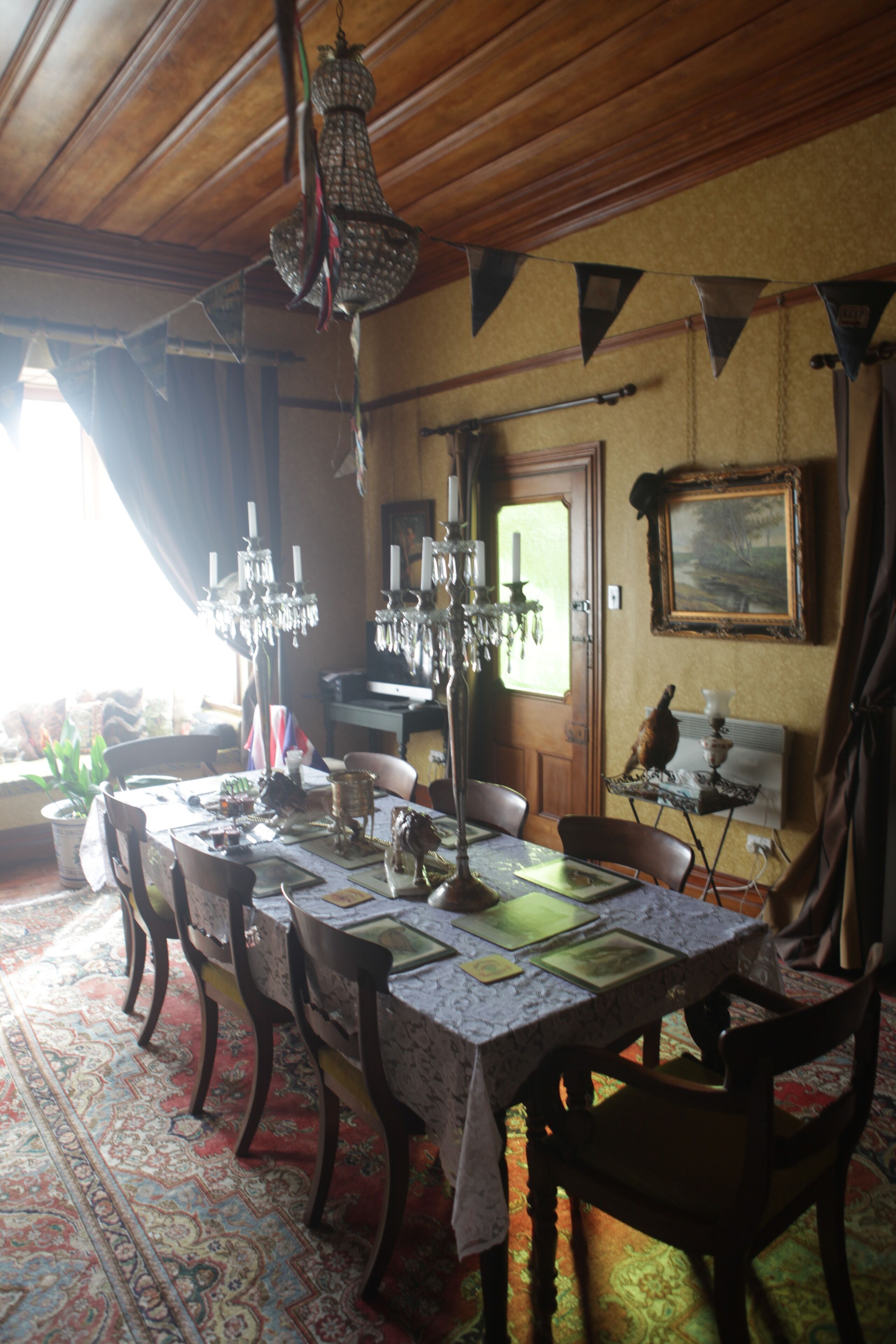 Comedor con techo de madera, candelabro, mesa lista para cuatro personas y alfombra con diseño.