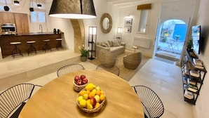 A modern kitchen with a bar area, a dining table with fruit bowls, a sofa, and a bookshelf. - Croce Luxury Apartment with Air Conditioning, Wi-Fi n0975 (Siracusa)