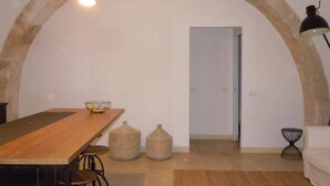 Ein Zimmer mit einem Holztisch, einer Hängelampe, einem gewebten Korb und einer Tür zu einem weiteren Raum.