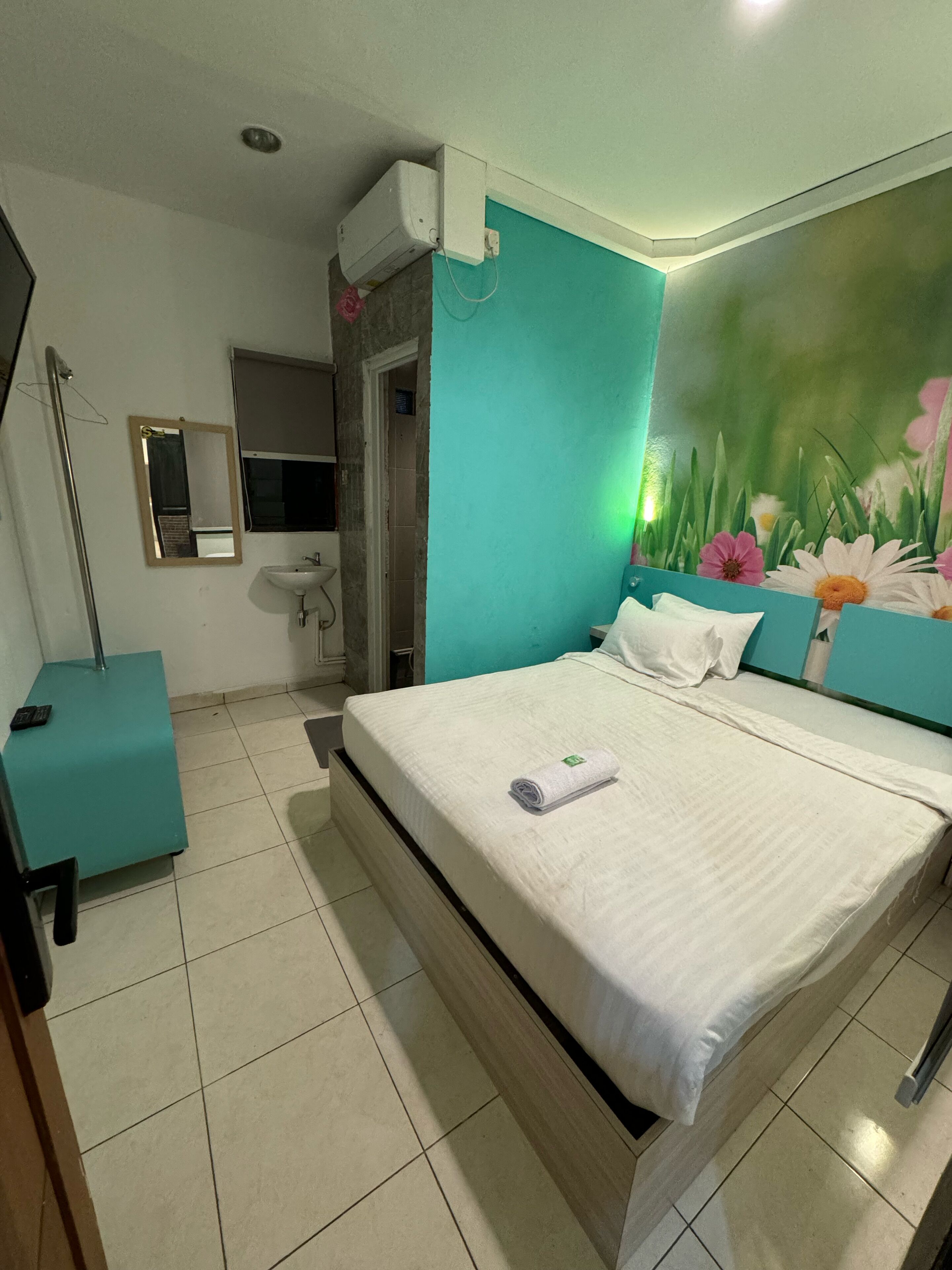 A bedroom with a bed, a bedside table, a mirror, a sink, and a door leading to another room.
