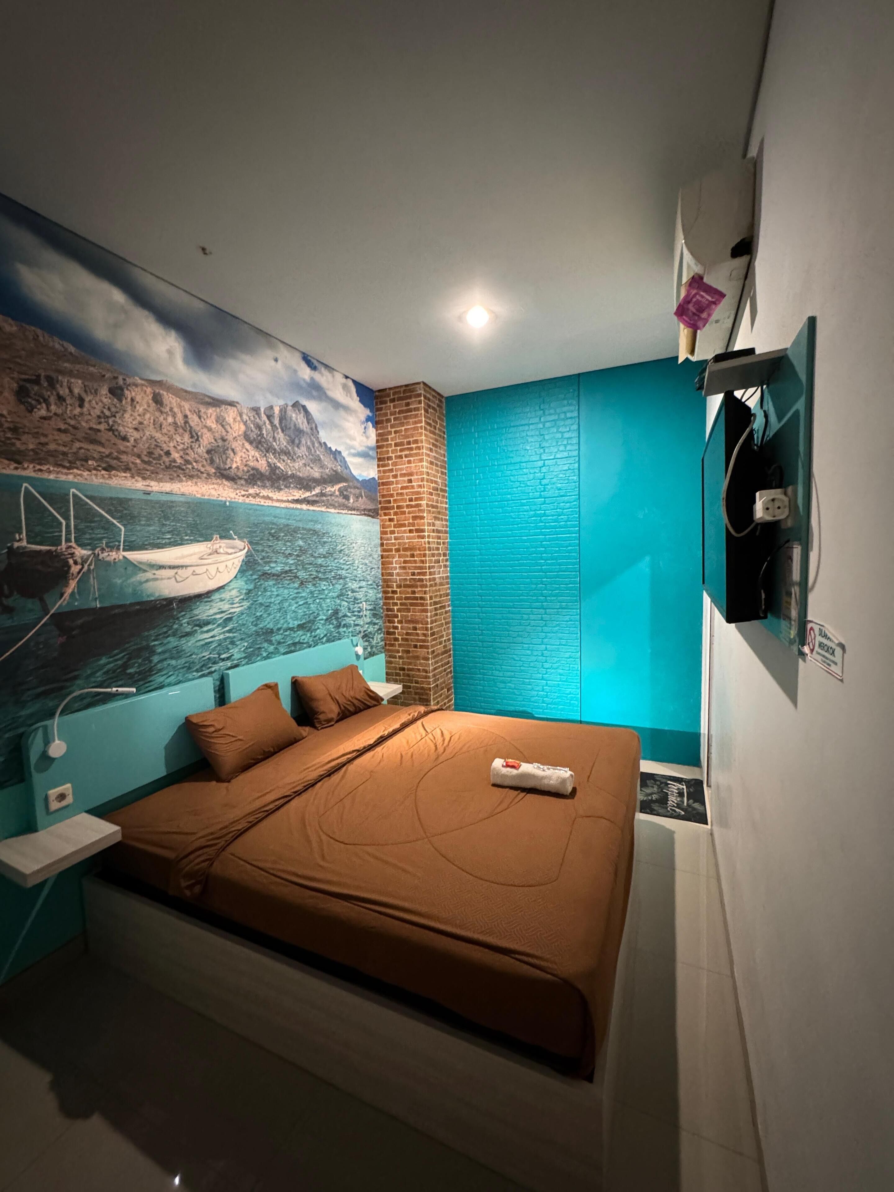 A bedroom with a bed, a nightstand, a wall-mounted TV, and a mural of a boat on water.
