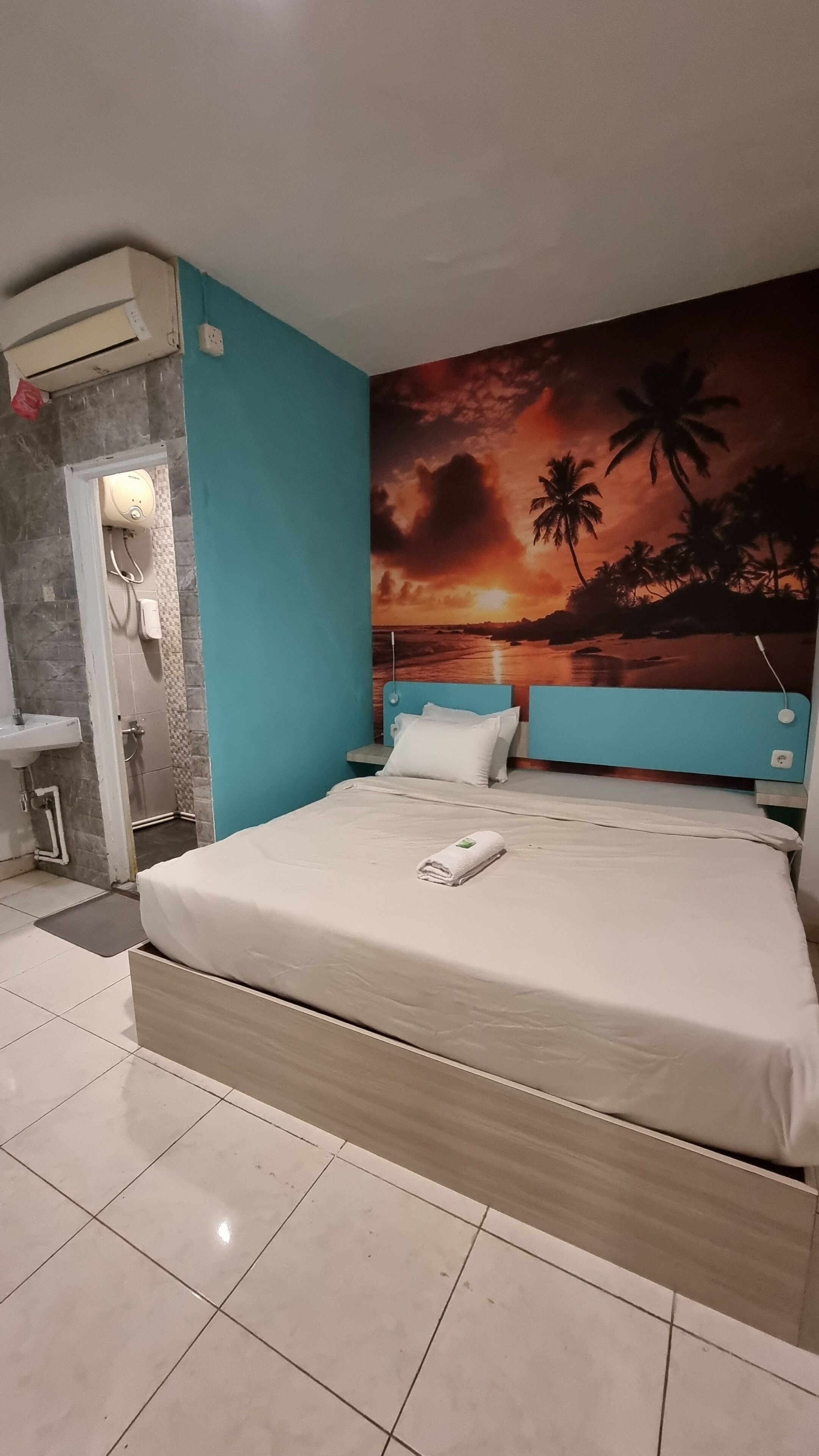 A hotel room with a bed, a bathroom, and a mural of a sunset over the ocean.