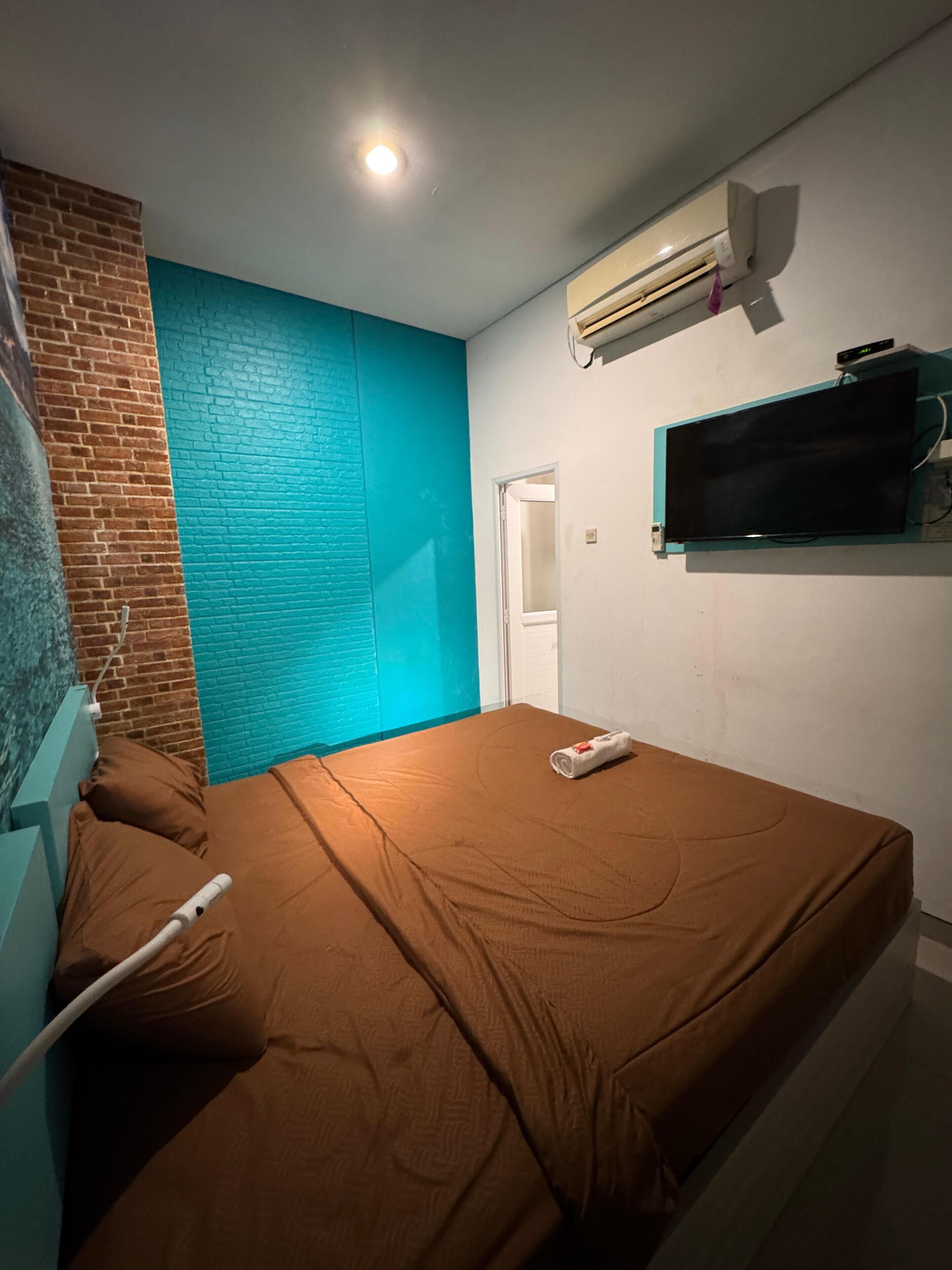A bedroom with a brick wall, a teal accent wall, a flat-screen TV, and a bed with brown bedding.